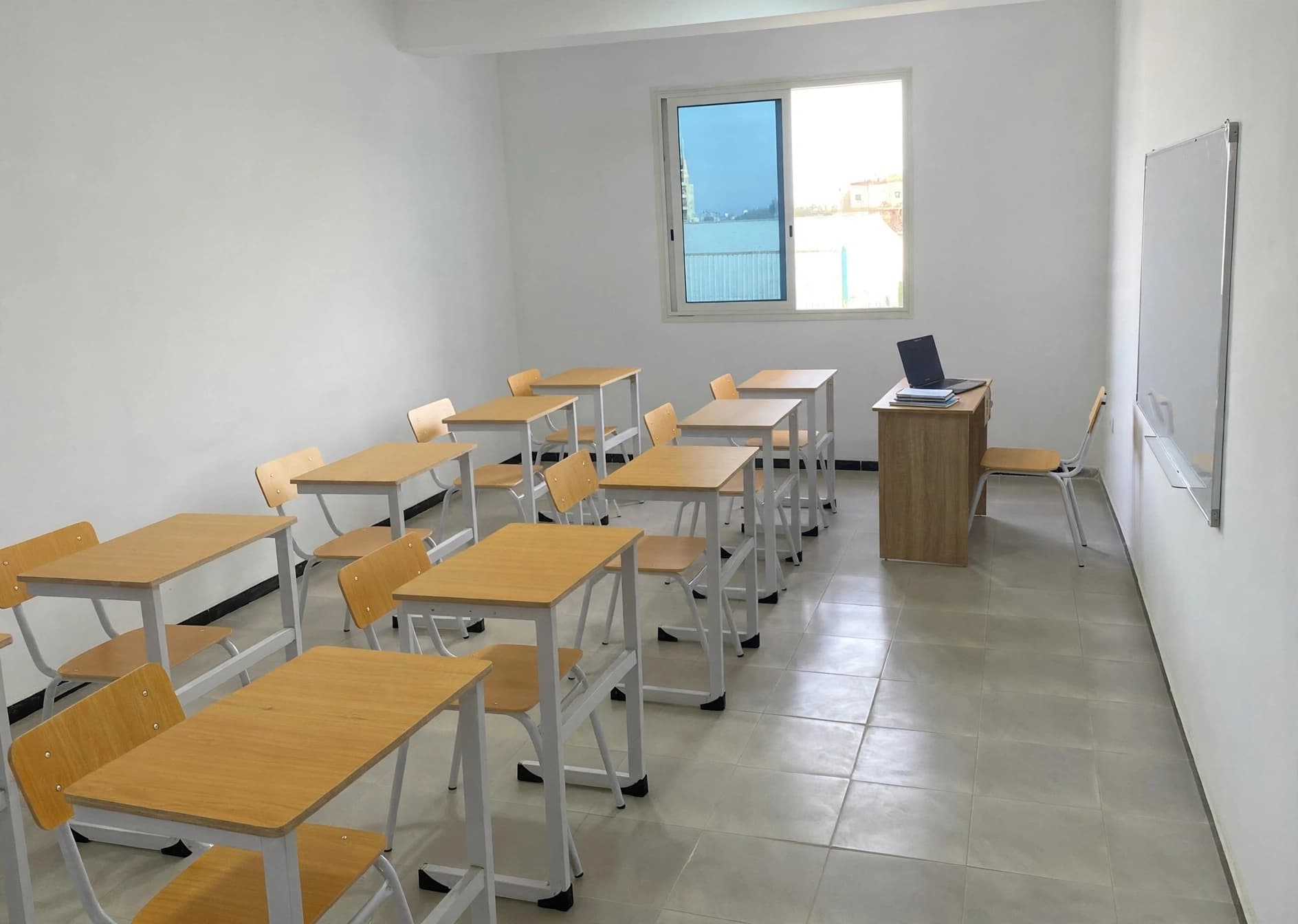 Salle de classe ZAD en présentiel : rangées de tables en bois, bureau de l'enseignant et tableau blanc